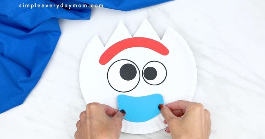 Hands attaching the blue mouth piece to a paper plate Forky craft.