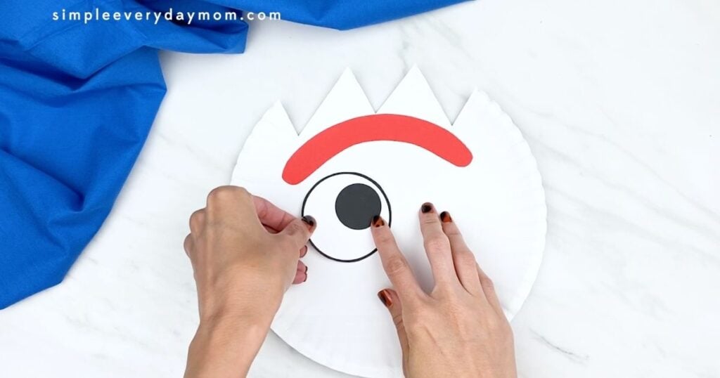 Hands placing the first eye onto a paper plate Forky craft.