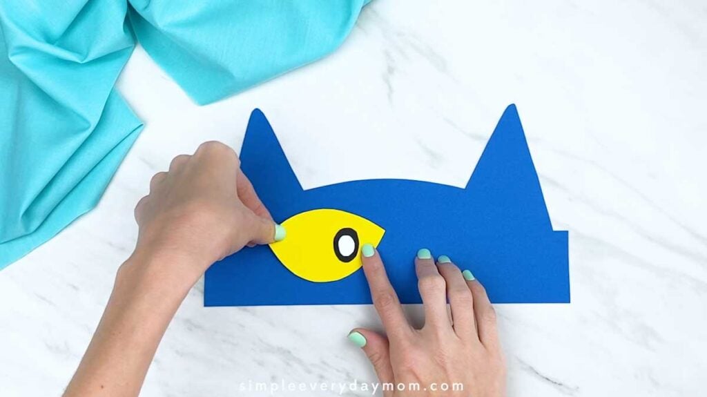Hands placing a completed yellow eye onto the blue cat headband base.