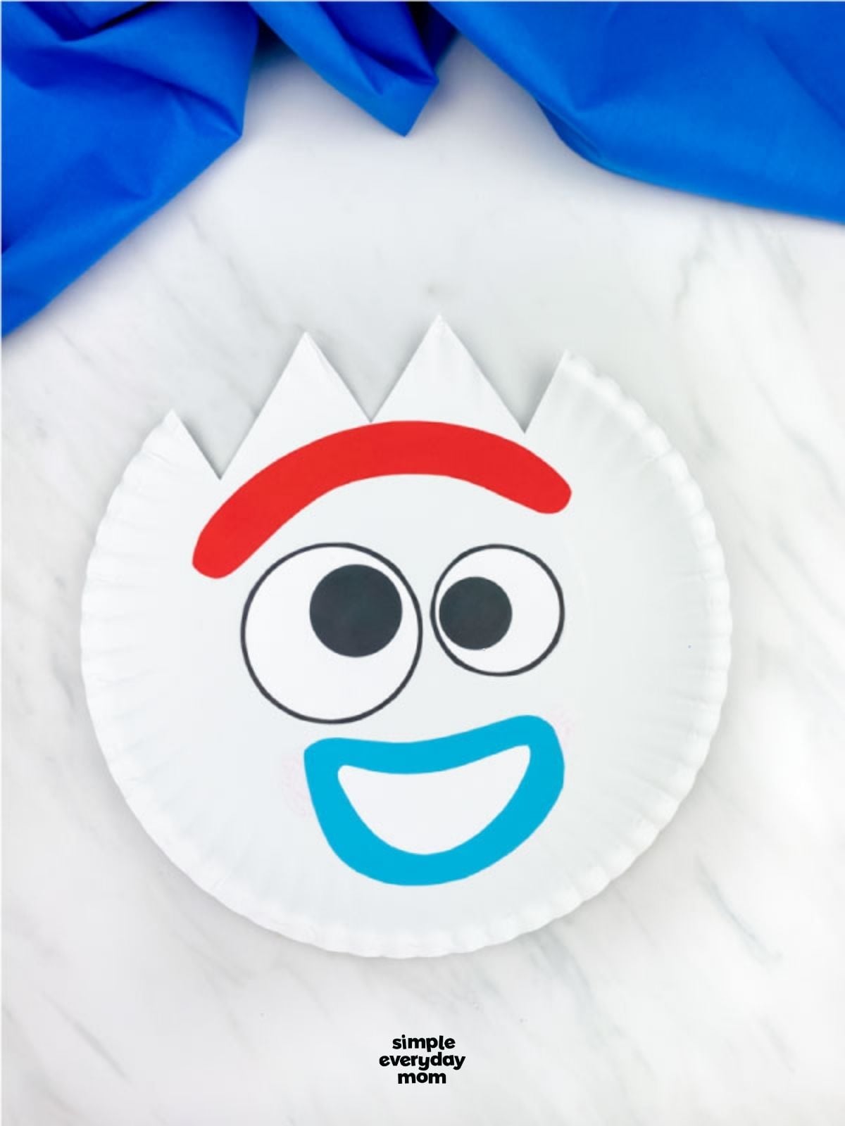 Paper plate craft of Forky with a smiling expression, made with printed eyes, a red eyebrow, and blue smile.