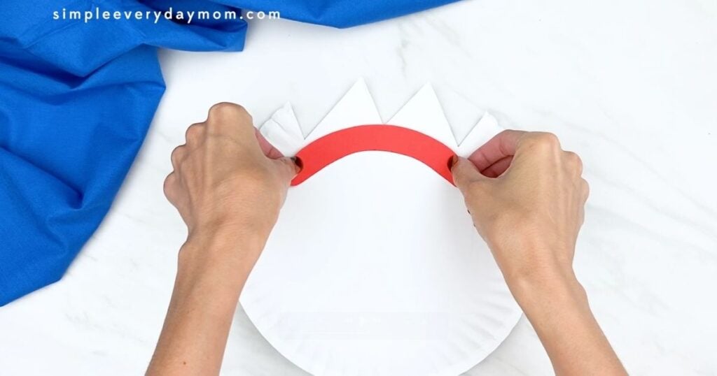 Hands attaching the red eyebrow piece to a paper plate for a Forky craft.