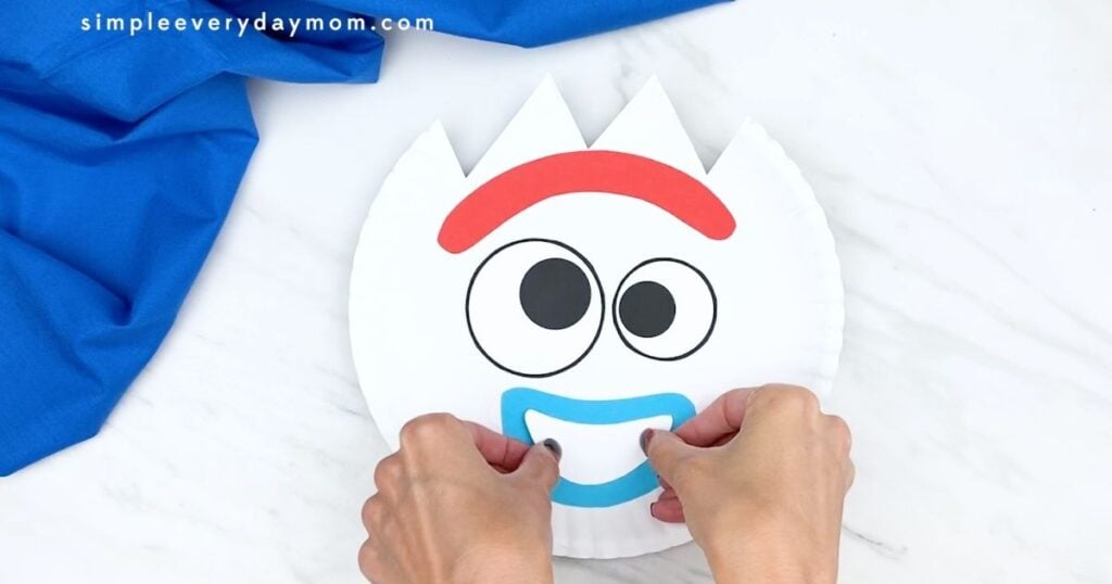 Hands attaching the white smile insert to complete the Forky paper plate craft.