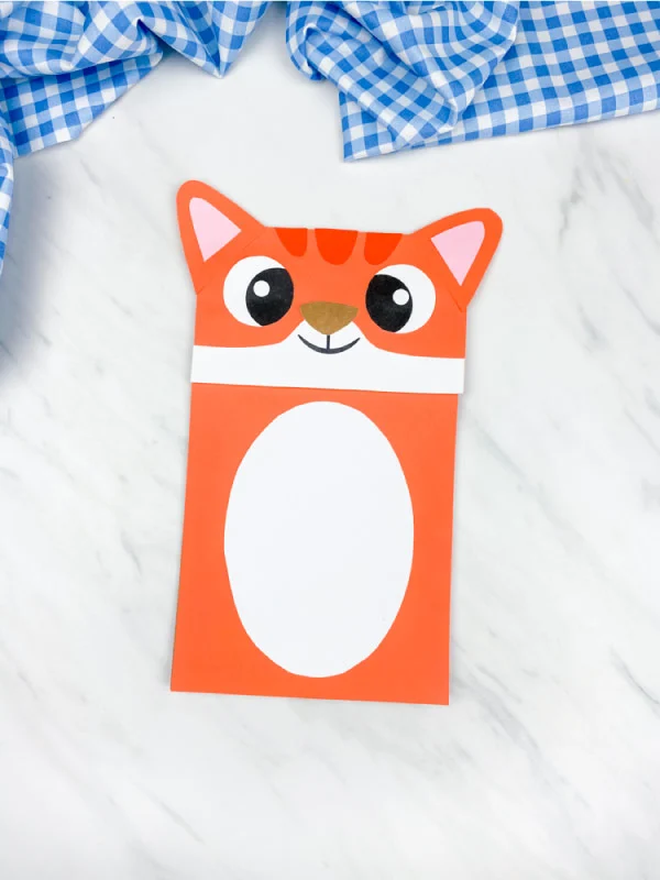 orange paper bag cat craft on marble background with blue checkered fabric