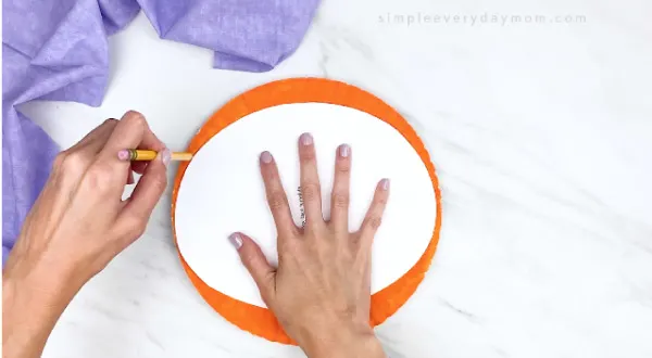 hands tracing fox template onto orange paper plate 