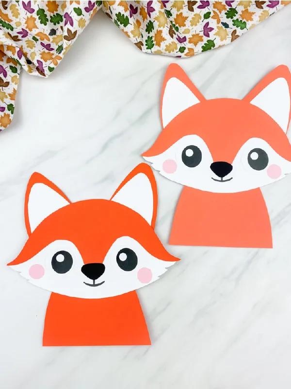 closeup image of two paper fox crafts  on marble background with leaf print fabric