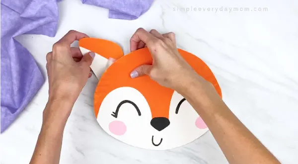 hands taping paper plate fox ear to back of paper plate 