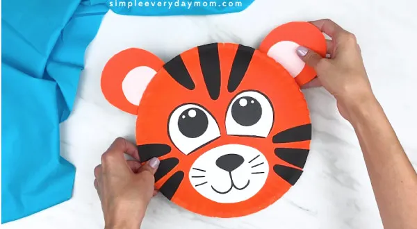hands gluing tiger ear to back of paper plate tiger 