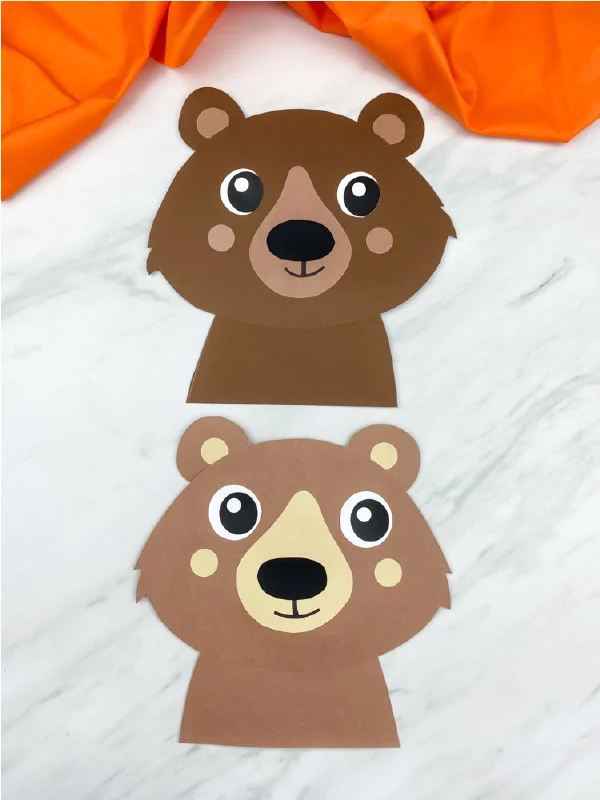 two completed paper bear crafts on marble background with orange fabric. Top bear is dark brown, bottom bear is light brown 