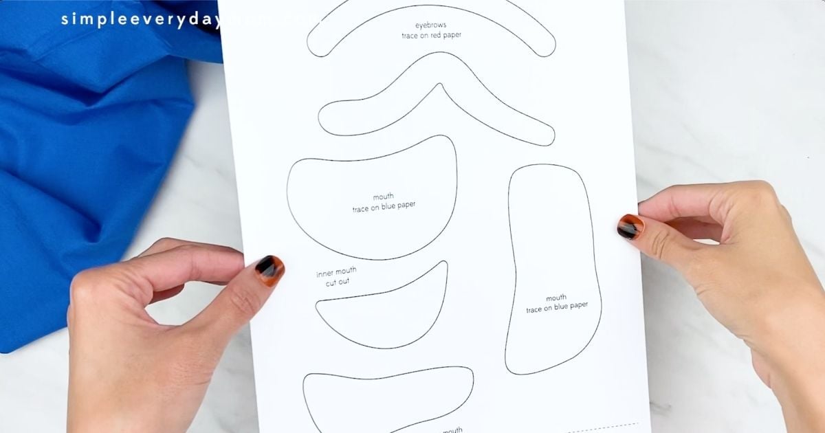 Hands holding the printable template pieces for the Forky paper plate craft before cutting them out.