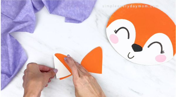 hands gluing inner ear to outer ear with paper plate fox on right side 