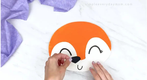 hands gluing black nose onto orange paper plate fox 