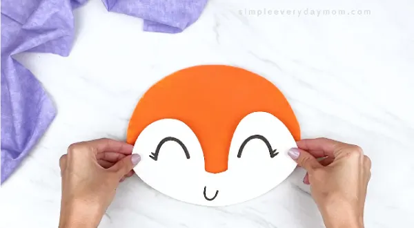 hands gluing fox face onto orange paper plate 