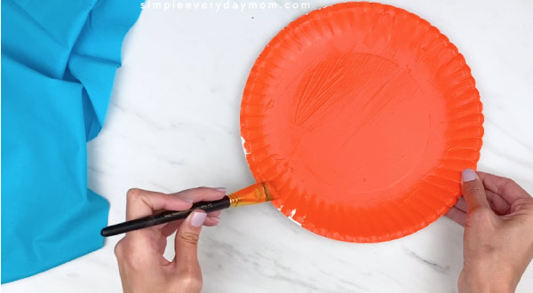 hands painting paper plate orange