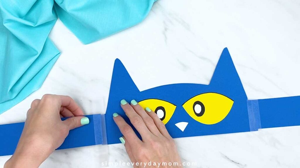 Hands attaching a second blue strap to complete the cat headband.