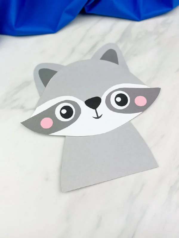 one  completed paper raccoon crafts on marble background with blue fabric 