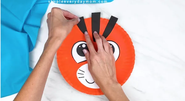 hands gluing on tiger stripes onto orange paper plate 