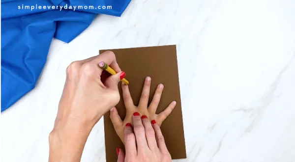 adult hand tracing child hand on brown paper 