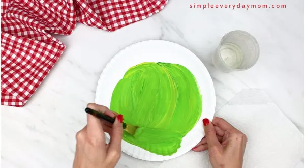 hands painting a paper plate green 