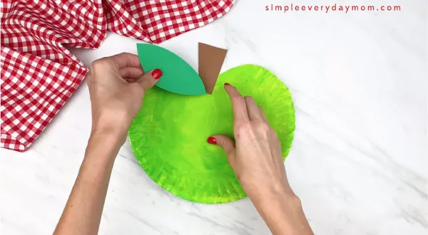 hands gluing on leaf on paper plate apple 