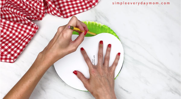 hands tracing apple template on top of paper plate