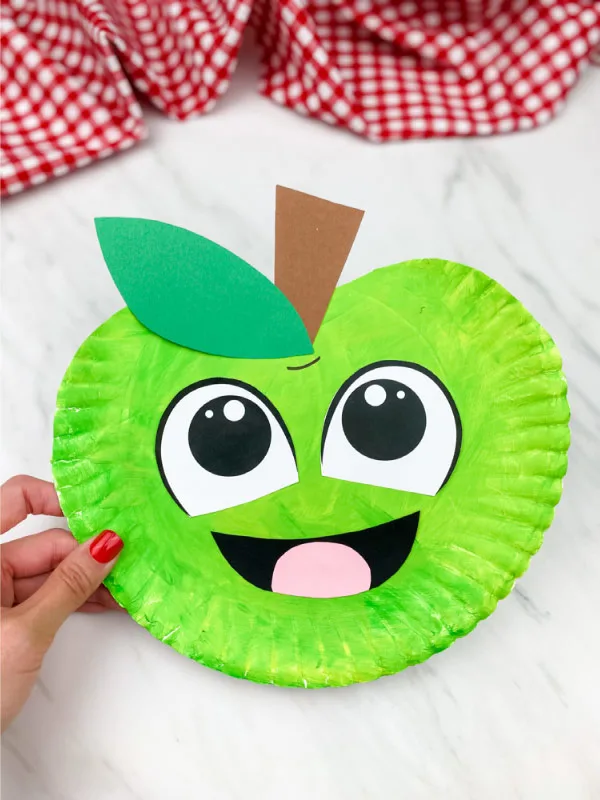 green paper plate apple craft on marble background with checkered fabric on top