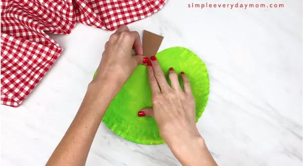 hands gluing on stem on paper plate apple 