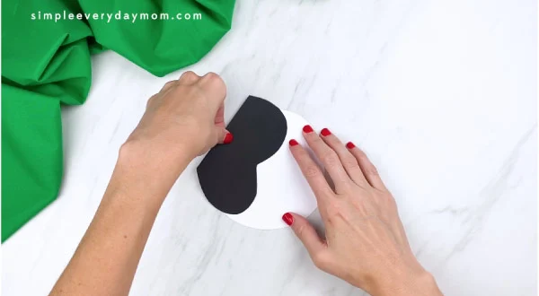 hands gluing black wavy paper to white paper 