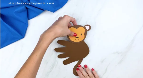 hands gluing tail to back of monkey handprint 