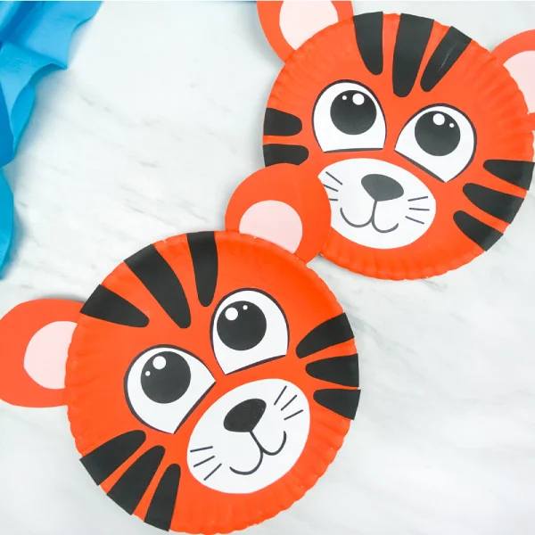 two paper plate tiger crafts on marble background with blue fabric 