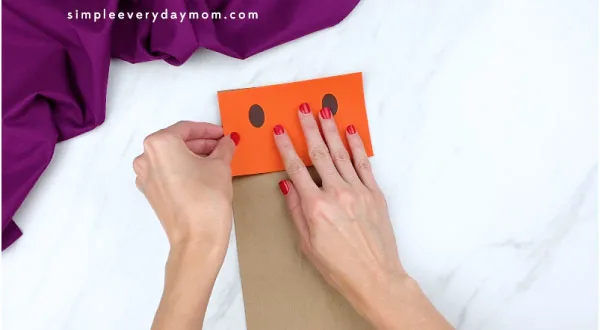hands gluing orange rectangle to paper bag flap 