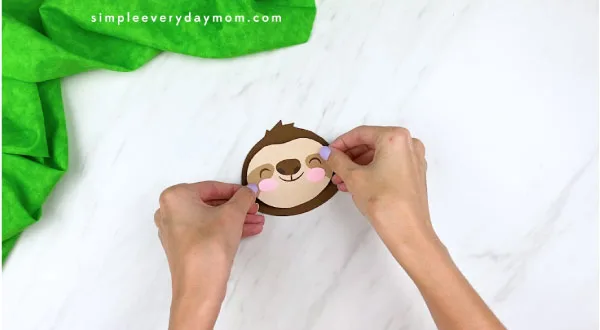 hands gluing sloth face to head