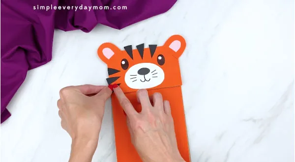 hands gluing tiger stripes to paper bag tiger face 