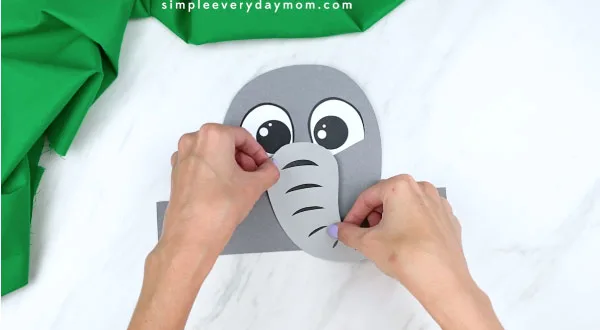 Hands gluing elephant trunk to paper elephant head