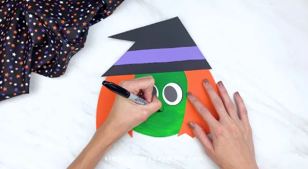 hands drawing on nose and mouth on paper plate witch