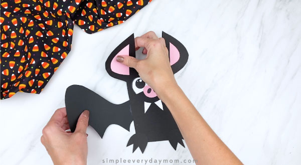 hands gluing wings to back of paper bat craft