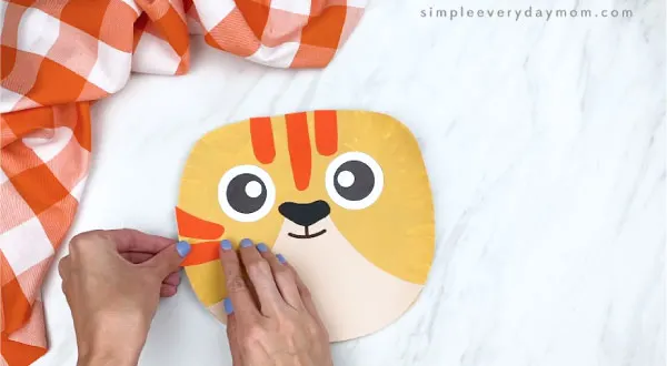hands gluing orange stripes onto paper plate tabby cat craft