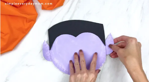hands gluing ears onto vampire paper plate craft