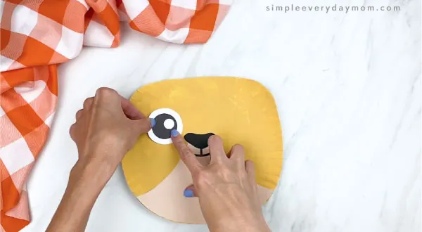 hands gluing eye onto paper plate cat craft