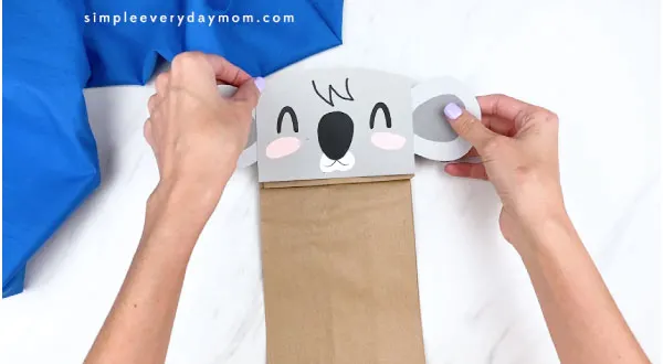 Hands gluing koala face to brown paper bag