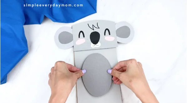 Hands gluing gray belly to paper bag koala craft