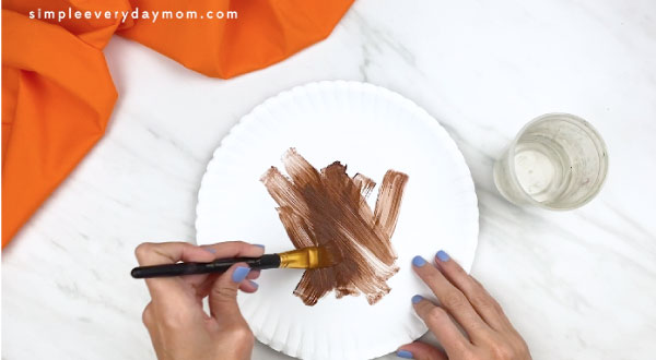 hands painting white paper plate brown