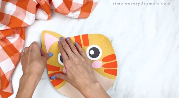hands gluing ears to back of paper plate cat craft