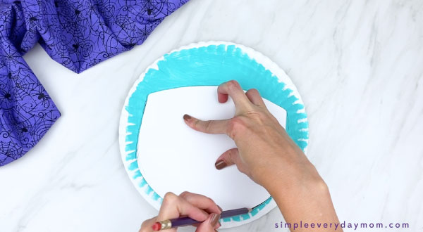 hands tracing mummy face template onto paper plate