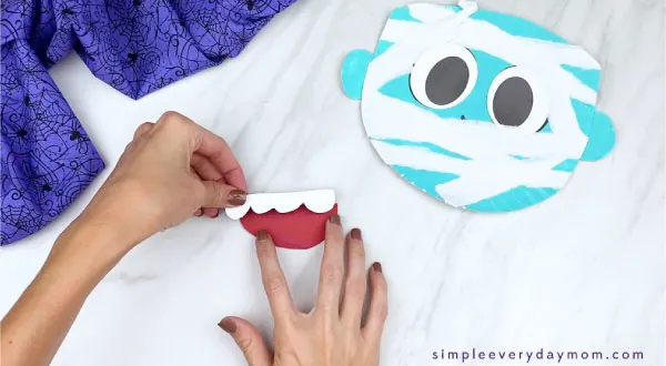 hands gluing teeth onto paper plate mummy mouth