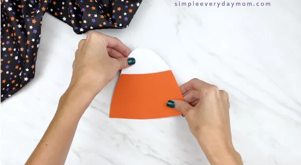 hands gluing top of paper candy corn craft together