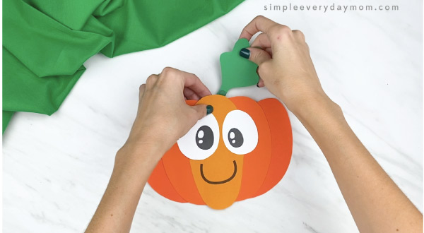 hands gluing leaf to top of paper pumpkin
