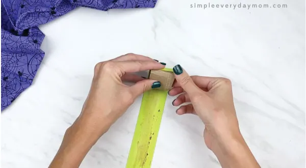 hands gluing green paper to toilet paper roll spider