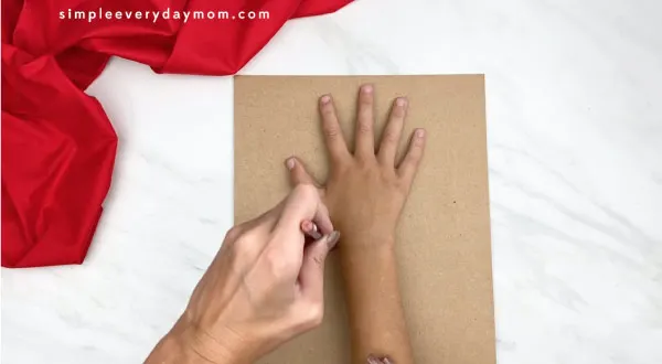 adult hand tracing child hand on brown paper
