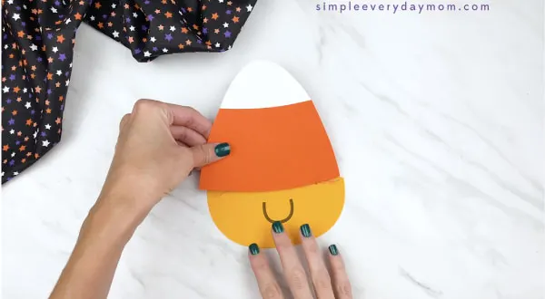 hands gluing paper candy corn craft body together