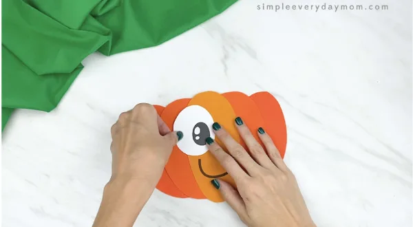 hands gluing eyes to paper pumpkin craft